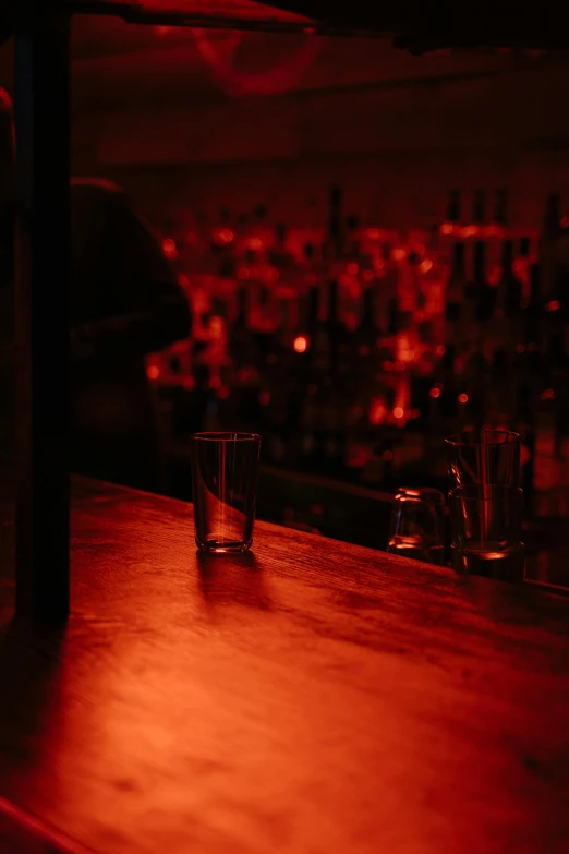 a bottle of alcohol sitting on top of a wooden bar, unsplash, red light, an empty backroom at night, flares