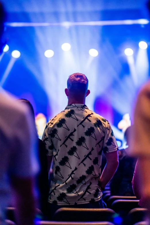 a man standing in front of a crowd of people, patterned clothing, nightlife, from the back, manly