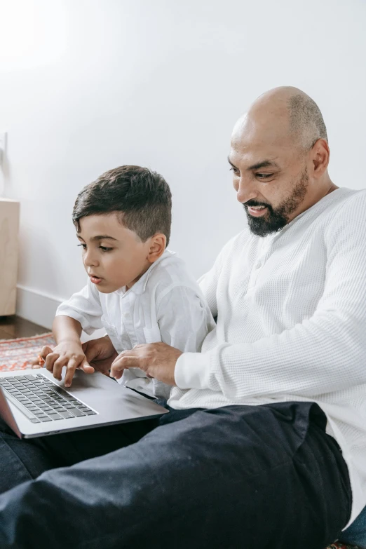 a man and a boy sitting on the floor with a laptop, slightly pixelated, te pae, thumbnail, father figure image