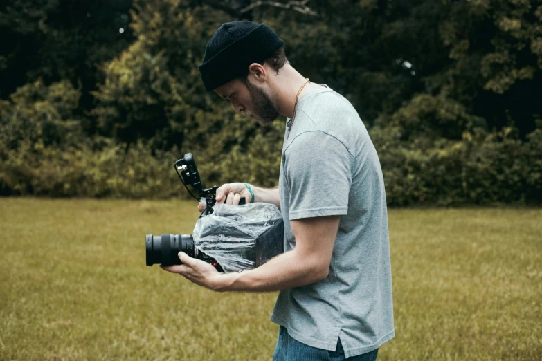 a man standing in a field holding a camera, fluid bag, phantom grip, mr beast, carson ellis