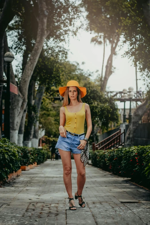 a woman wearing a yellow top and blue shorts, a colorized photo, by Robbie Trevino, pexels contest winner, tlaquepaque, wearing a hat, marbella, yellow-orange