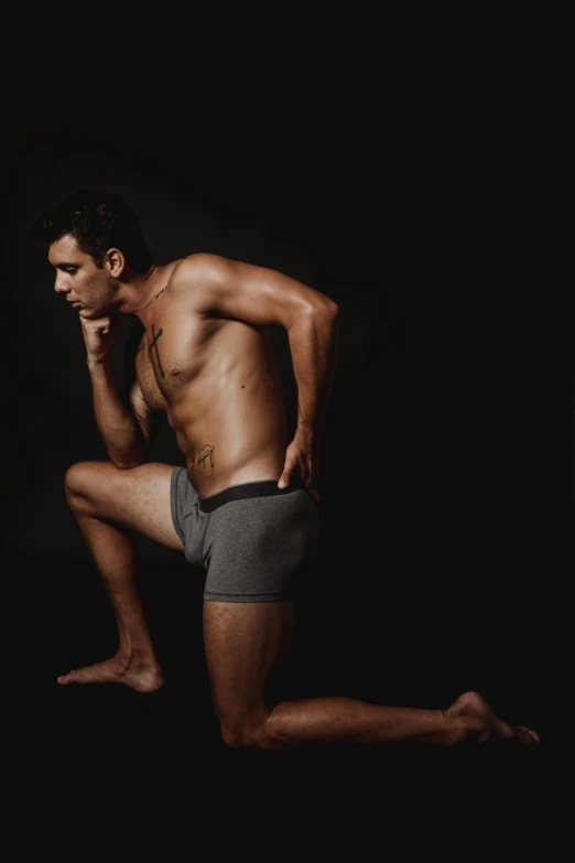 a man in underwear sitting on the ground, a colorized photo, inspired by Nathan Oliveira, on black background, promo image, kneeling, grey