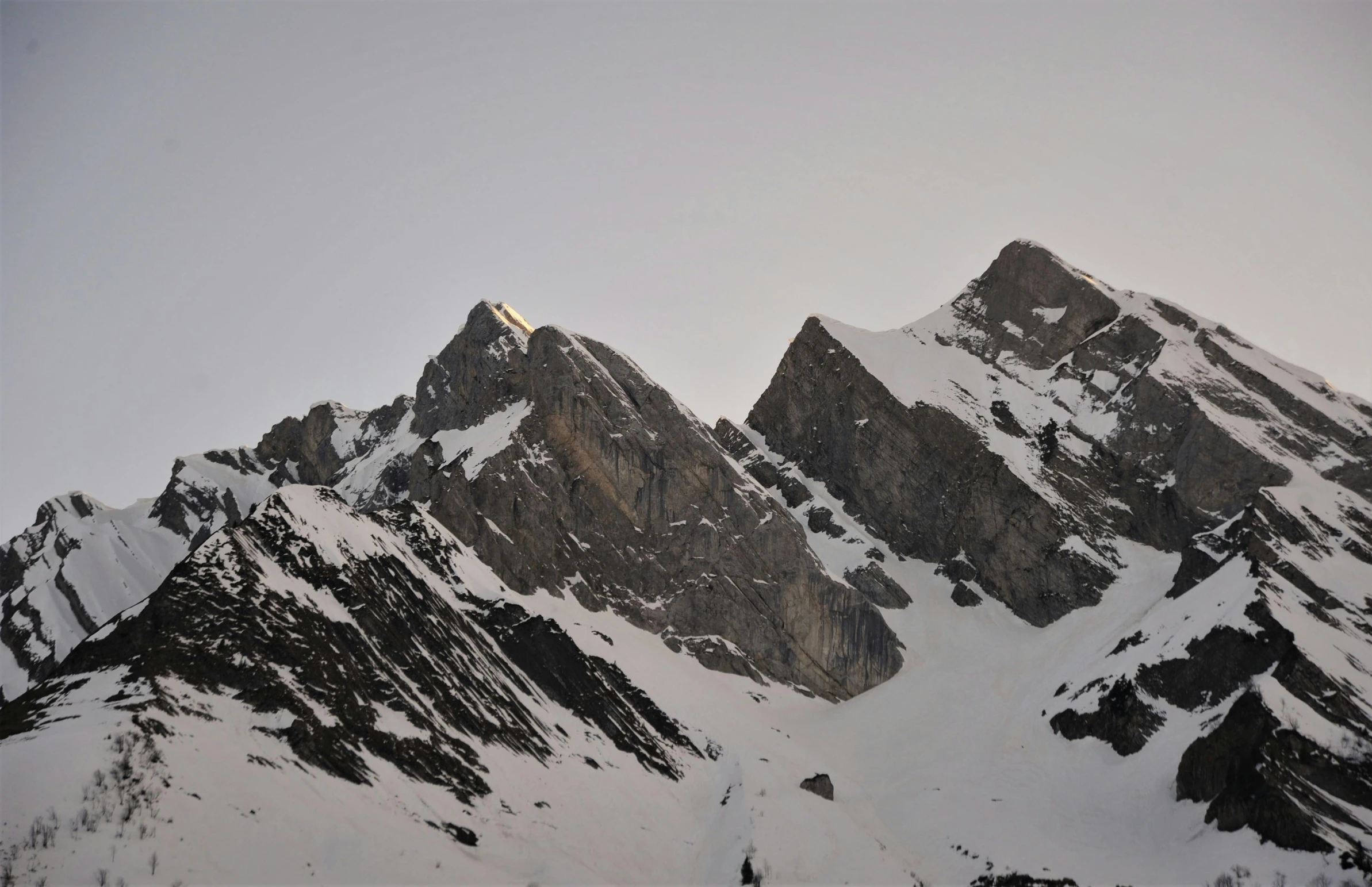 a group of people riding skis down a snow covered slope, large rocky mountain, tall mountain, evening lighting, markarth