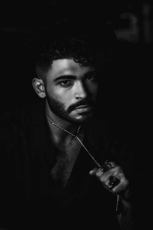 a black and white photo of a man in the dark, an album cover, by Alexis Grimou, trending on pexels, photorealism, arab man light beard, wearing a bandana and chain, a handsome man，black short hair, lily frank