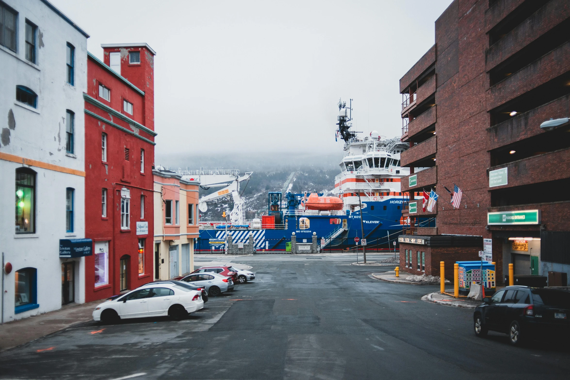 a white car driving down a street next to tall buildings, a photo, by Brian Snøddy, pexels contest winner, hyperrealism, ships in the harbor, antarctic, picton blue, red building