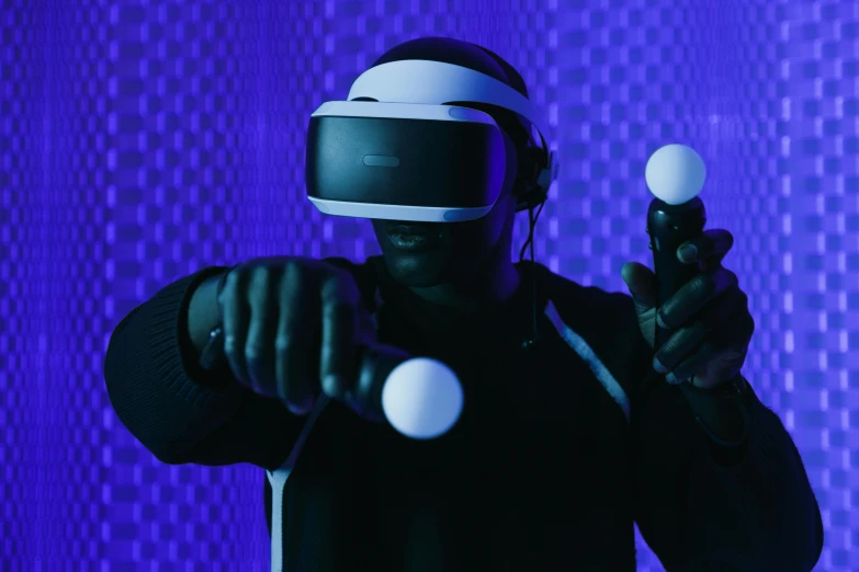 a man in a black shirt holding a video game controller, a hologram, inspired by Beeple, unsplash, interactive art, dark blue spheres fly around, : kanye west wearing vr goggles, dramatic white and blue lighting, purple ambient light