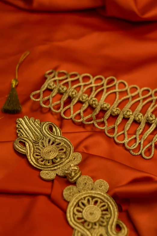 a close up of a necklace on a red cloth, an album cover, by Thomas Furlong, flickr, baroque, intricate gold headdress, cords, embroidered uniform guard, award-winning style