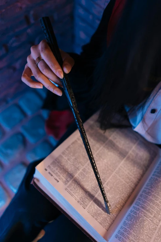 a person holding a pen and a book, holding the elder wand, lit up, lurking, up-close