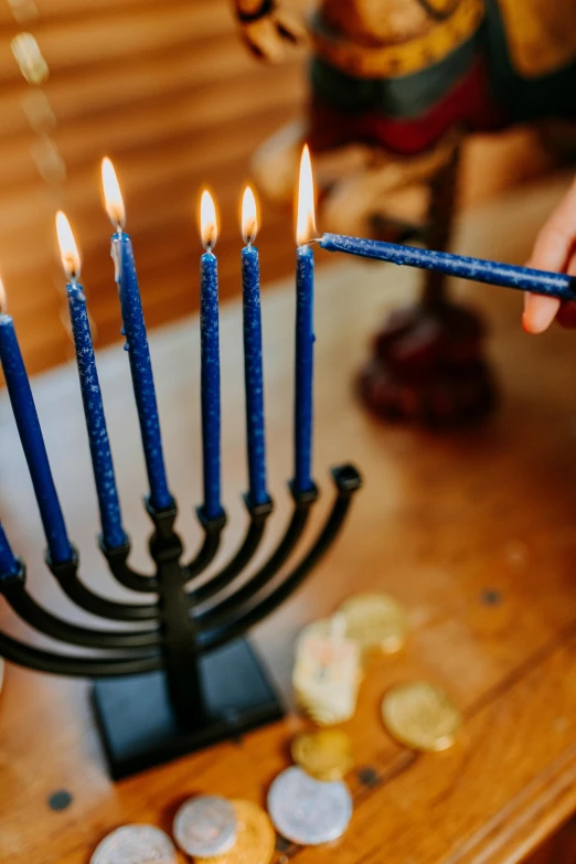 a person lighting a menorah with lit candles, by Julia Pishtar, fine art, indigo, vivid), holiday, a wooden