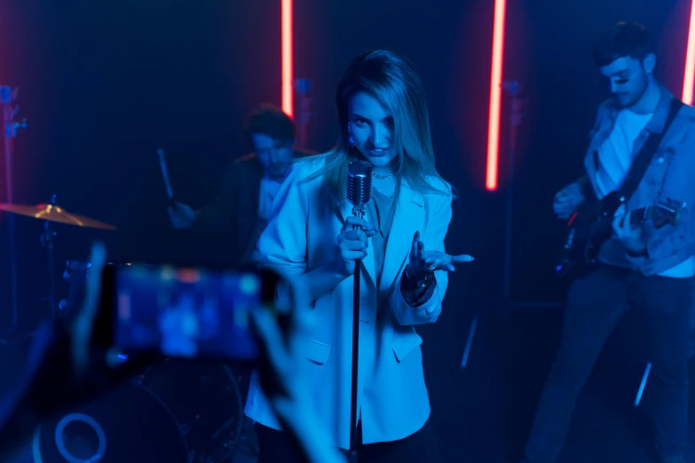 a woman that is standing in front of a microphone, an album cover, pexels, happening, performing a music video, smartphone footage, high blue lights, behind the scenes photo