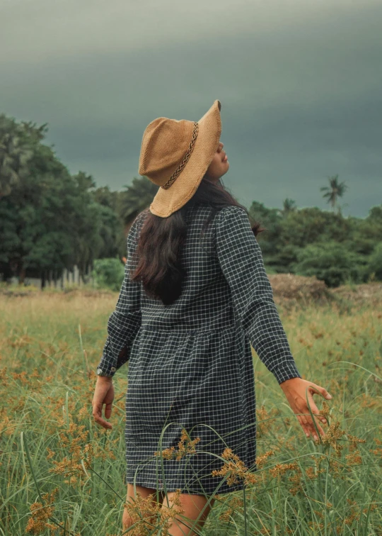 a woman standing in a field of tall grass, inspired by Ruth Jên, pexels contest winner, straw hat and overcoat, assamese aesthetic, profile image, backfacing