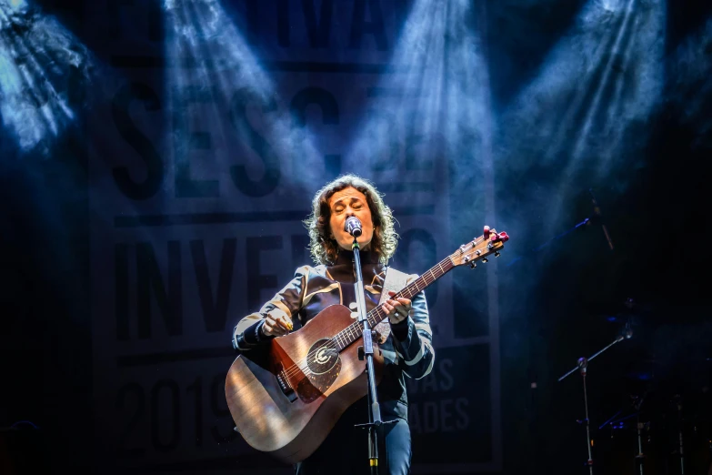 a man holding a guitar on top of a stage, inspired by Eva Gonzalès, pexels contest winner, private press, elaine benes, looking towards the camera, university, rebecca sugar