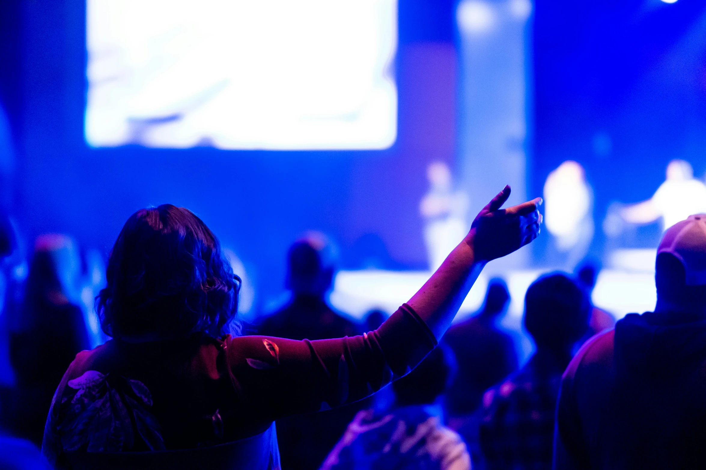 a group of people that are standing in front of a screen, worshipers, blue, pointing, nightlife