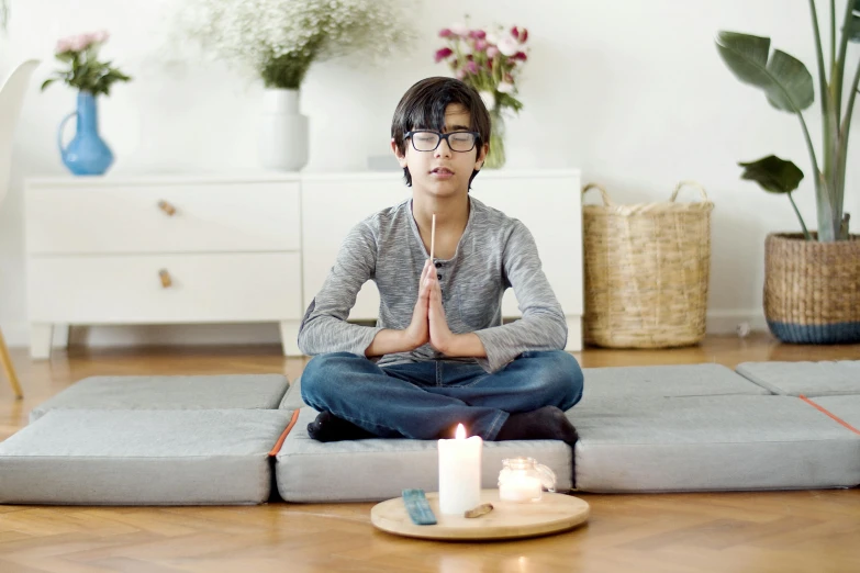 a woman sitting on a yoga mat in front of a lit candle, by Nina Hamnett, pexels, hurufiyya, in square-rimmed glasses, teen boy, meditating pose, avatar image