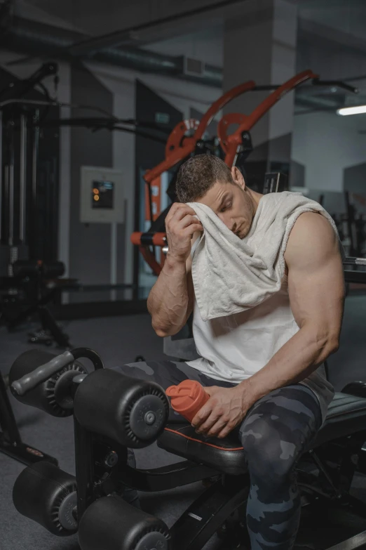 a man wiping his face while sitting on a bench in a gym, a colorized photo, by Adam Marczyński, pexels contest winner, wearing a muscle tee shirt, gif, thicc, covered in