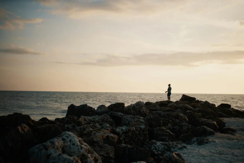 a man standing on top of a rocky beach next to the ocean, people angling at the edge, unsplash photography, multiple stories, a person standing in front of a