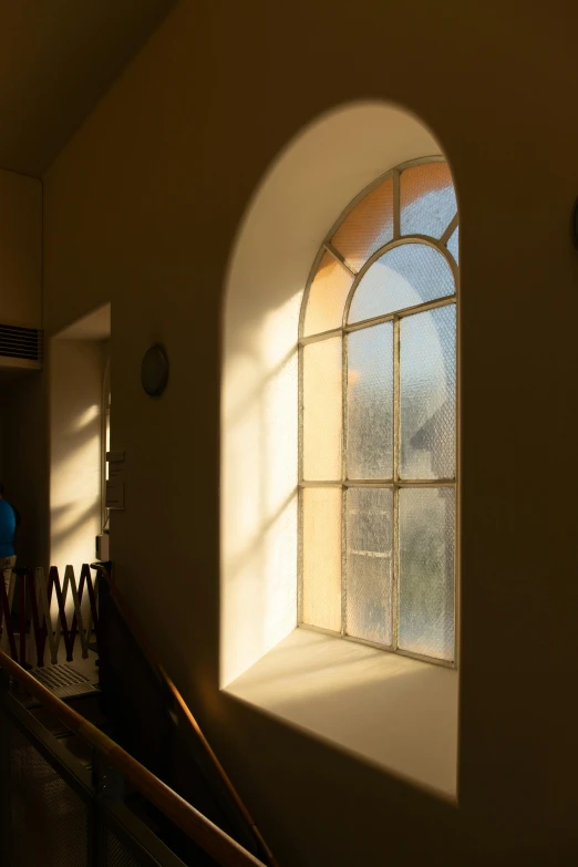 a man standing next to a window in a building, inspired by William Nicholson, light and space, the narthex, golden hour sun, bay window, curved hallways