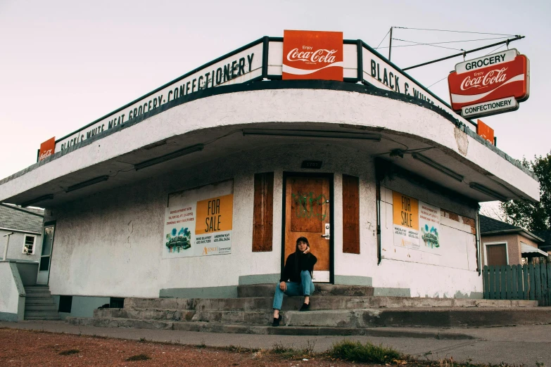 a man that is standing in front of a building, by Lee Loughridge, pexels contest winner, convenience store, sitting on the ground, nettie wakefield, new mexico