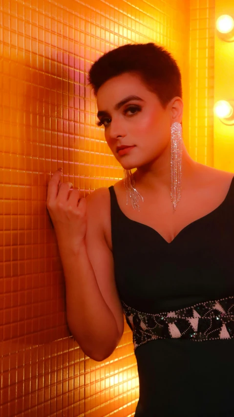 a woman in a black dress leaning against a wall, an album cover, by Robbie Trevino, pexels, lucy hale, huge earrings and queer make up, dazzling lights, thumbnail