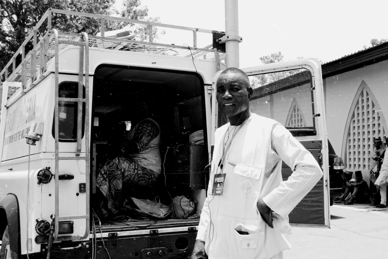 a black and white photo of a man standing in front of a truck, by Caroline Mytinger, hurufiyya, ambulance, adebanji alade, with everything in its place, very vibrant