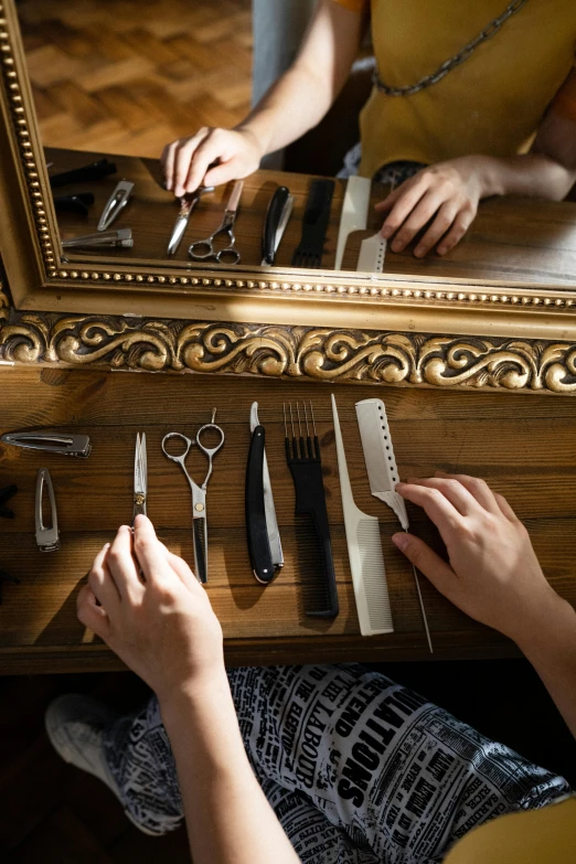 a woman that is sitting in front of a mirror, a still life, trending on pexels, arts and crafts movement, scissors, professional woodcarving, surgical implements, hands on counter