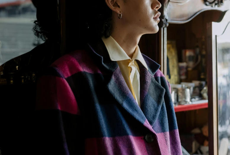 a woman standing in front of a window next to a clock, inspired by Clarice Beckett, unsplash, de stijl, wearing a purple smoking jacket, tartan garment, close up shot from the side, loose coat collar sailor uniform