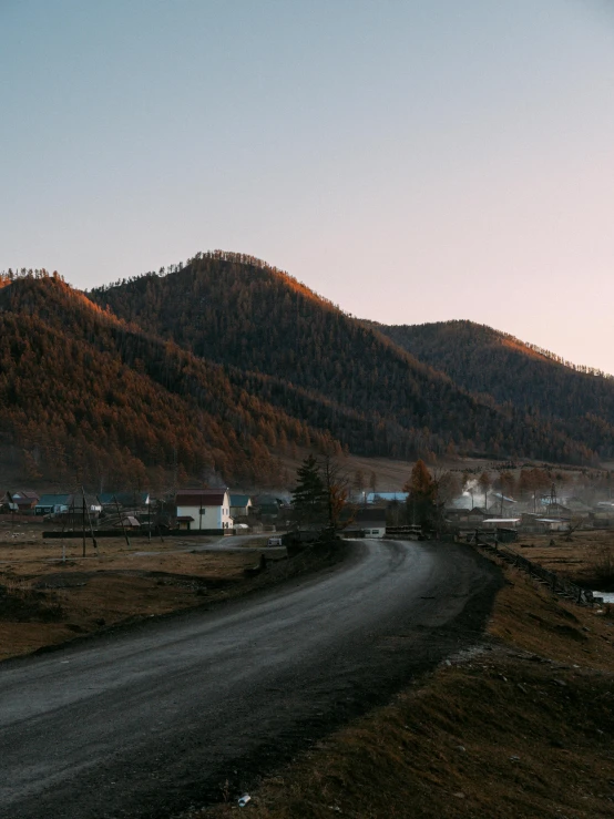 a dirt road with a mountain in the background, inspired by Konstantin Vasilyev, unsplash contest winner, ground level view of soviet town, at sunset in autumn, near lake baikal, grey