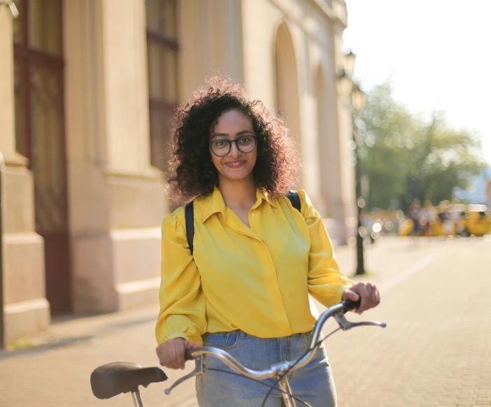 a woman standing next to a bicycle on a city street, pexels contest winner, wearing yellow floral blouse, avatar image, university, curly haired