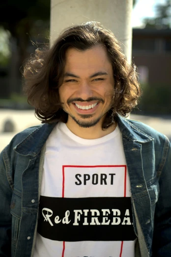 a man with long hair wearing a shirt that says sport red fireba, inspired by Eddie Mendoza, featured on reddit, non binary model, mutahar laughing, short goatee, nathan fielder