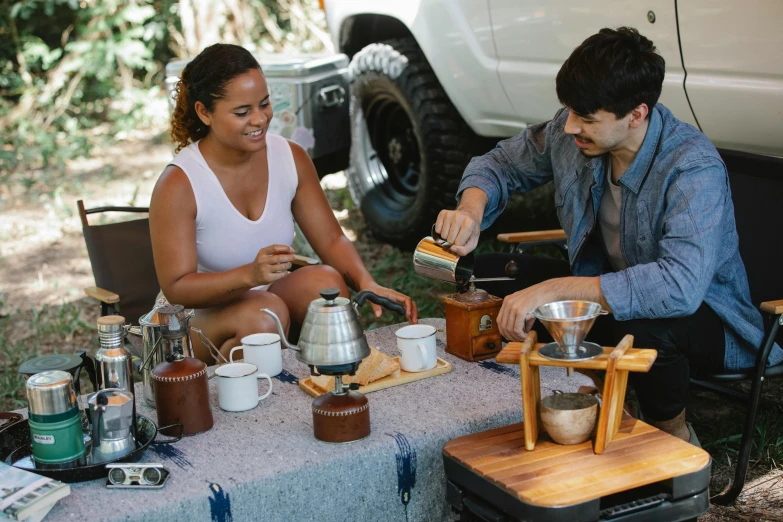 a man and a woman sitting at a picnic table, celebration of coffee products, kombi, cooking it up, brown