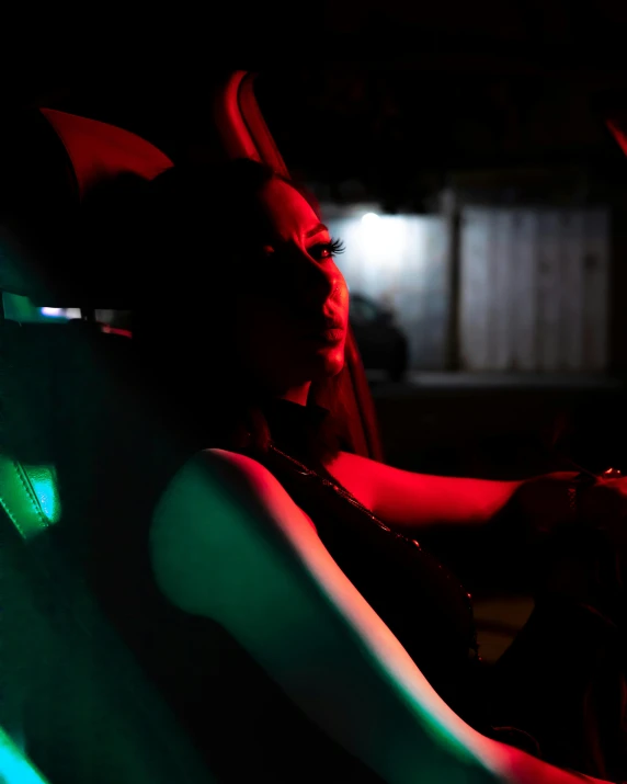 a woman sitting in the driver's seat of a car, inspired by Nan Goldin, unsplash, transgressive art, ariana grande as a sith, colored gels, tail lights, profile image