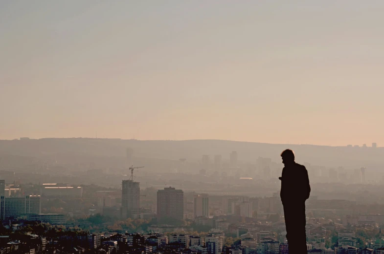 a person standing on top of a hill overlooking a city, by Attila Meszlenyi, pexels contest winner, a very sad man, still from a music video, aykut aydogdu, siluettes