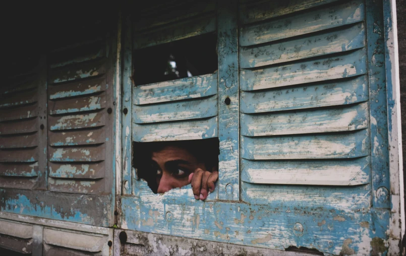 a close up of a person looking out of a window, a picture, shack close up, hiding behind obstacles, joel torres, eyes open