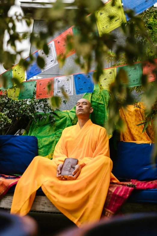 a man in a yellow robe sitting on a bench, unsplash, happening, prayer flags, next to a tree, green robes, shanghai