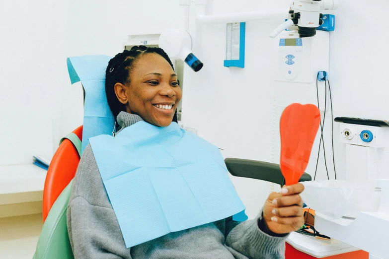 a woman sitting in a chair with a toothbrush in her hand, hurufiyya, large black smile, sterile colours, orange, healthcare worker