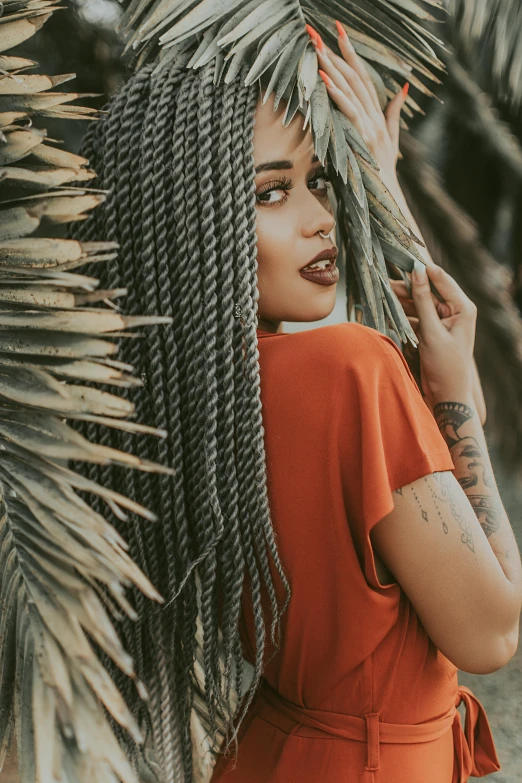 a woman standing in front of a palm tree, pexels contest winner, afrofuturism, photograph of a sleeve tattoo, hair texture, gray and orange colours, twisted braid