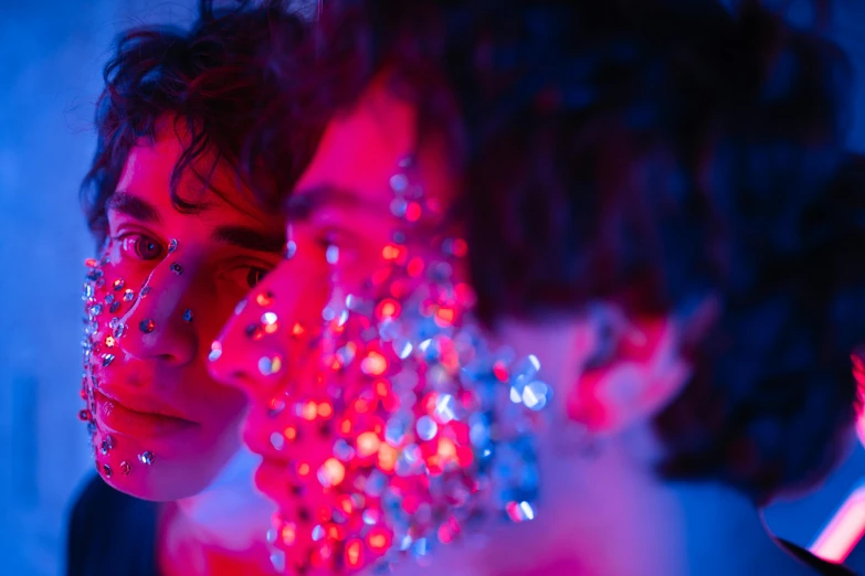 a couple of women standing next to each other, an album cover, by Adam Marczyński, pexels, skin made of led point lights, red blue, portrait of timothee chalamet, glitter makeup