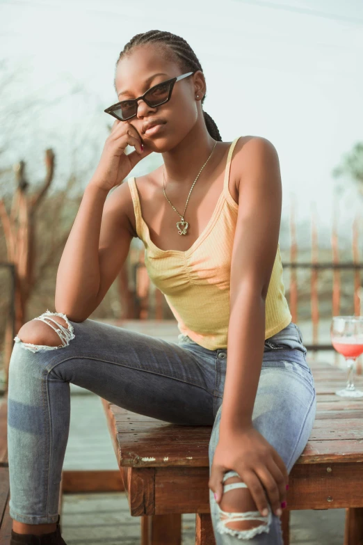 a woman sitting on a wooden table talking on a cell phone, by Stokely Webster, trending on pexels, wearing yellow croptop, ripped jeans, woman with rose tinted glasses, maria borges