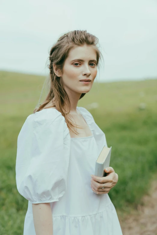 a woman standing in a field holding a book, inspired by Louisa Chase, renaissance, wearing white shirt, beautiful nordic woman, without makeup, promotional image