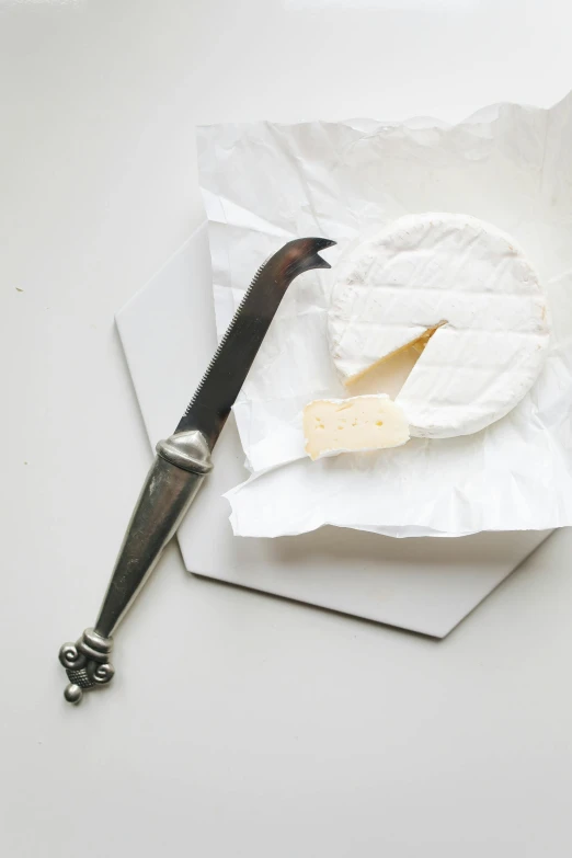 a knife sitting on top of a piece of paper next to a piece of cheese, white and silver, hexagonal shaped, product image, food