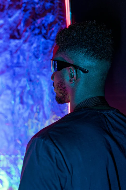 a man standing in front of a wall with neon lights, inspired by Frank Mason, trending on pexels, afrofuturism, wearing blue sunglasses, reflecting light in a nightclub, close up half body shot, 2 1 savage