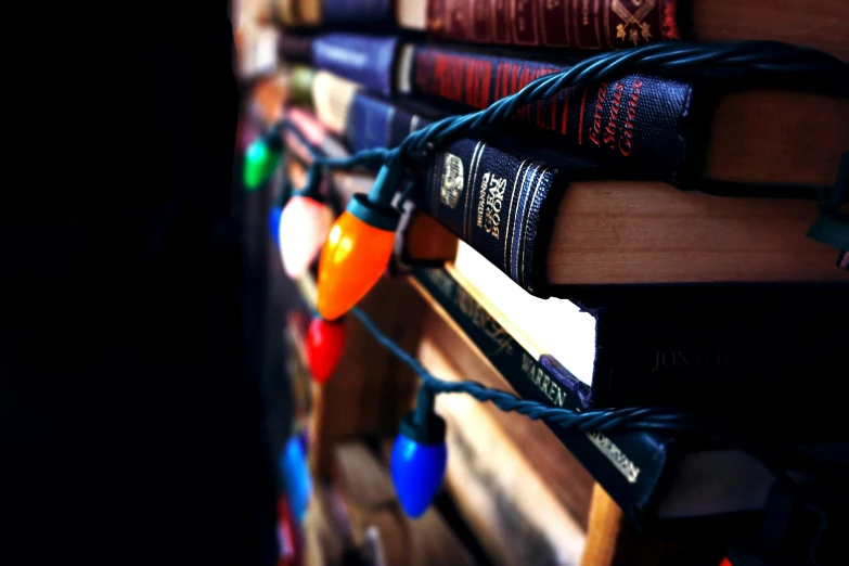 a bunch of books stacked on top of each other, a tilt shift photo, by David Donaldson, pexels contest winner, christmas lights, instagram post, gothic library, multicolored