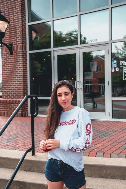 a beautiful young woman standing in front of a building, by Robbie Trevino, wearing sweatshirt, exiting store, at college, phalanster