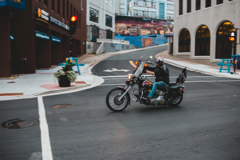 a man riding on the back of a motorcycle down a street, by Lee Loughridge, pexels contest winner, downtown, avatar image