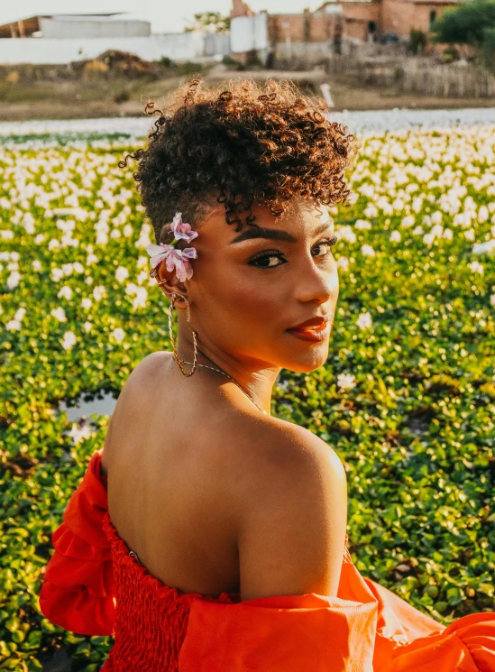 a woman sitting on top of a lush green field, an album cover, trending on pexels, happening, curly pixie cut hair, exotic lily ears, headshot profile picture, with flowers