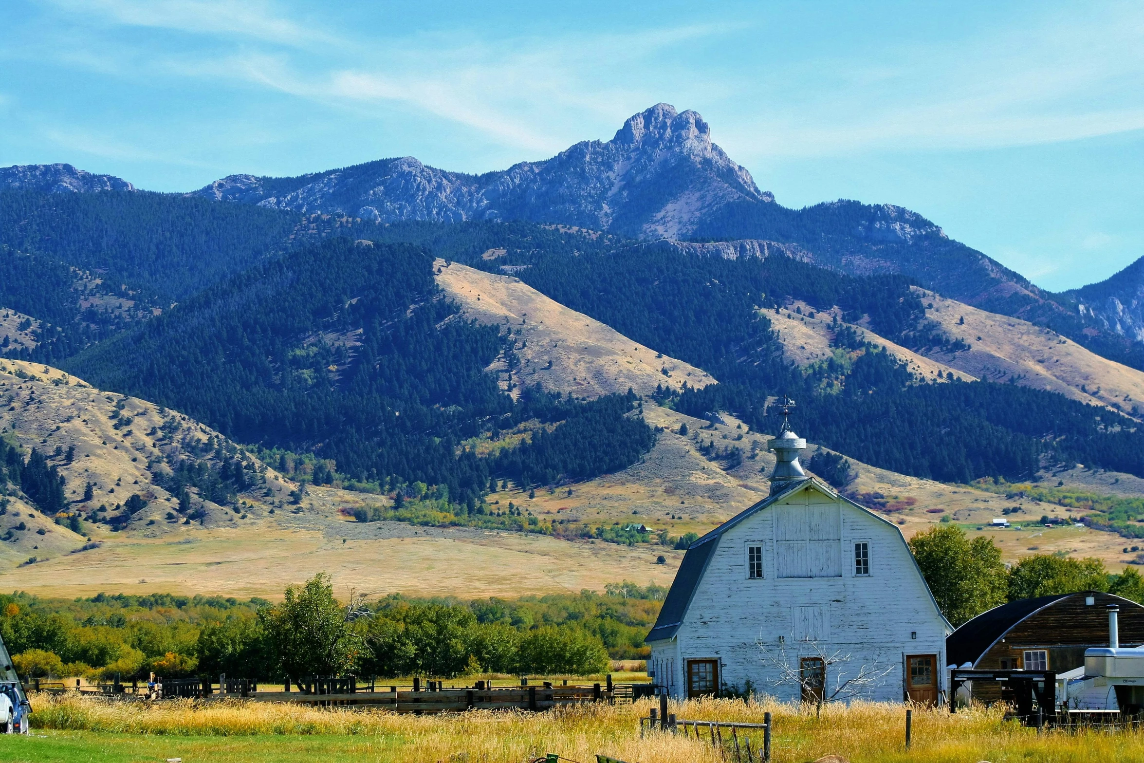 a white barn in a field with mountains in the background, by Jim Nelson, unsplash contest winner, renaissance, background image, montana, solo hiking in mountains trees, slightly tanned