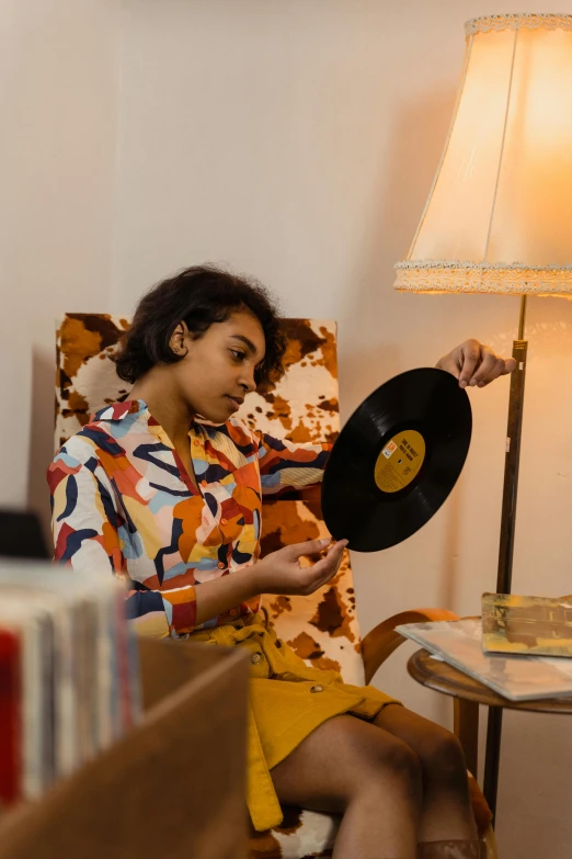 a woman sitting in a chair holding a record, trending on pexels, funk art, egypt, color photograph, brown, ashteroth