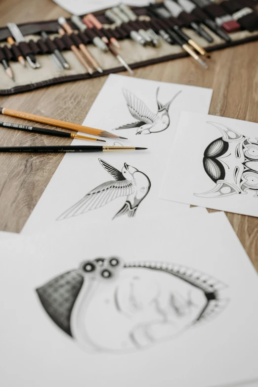 a bunch of drawings sitting on top of a wooden table, heads of wooden of bird face, pencils, detailed product shot, amanda lilleston