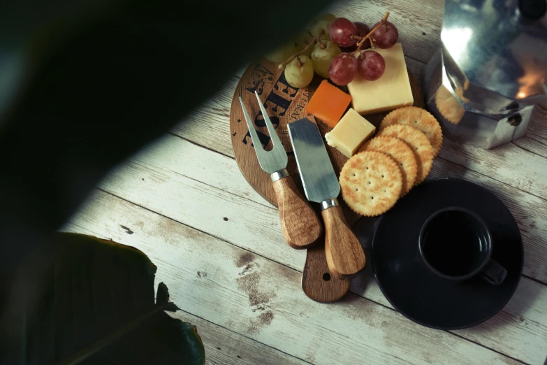 a plate of cheese, crackers and grapes on a table, a still life, inspired by Olive Mudie-Cooke, unsplash, shadows, on a wooden tray, cutlery, black