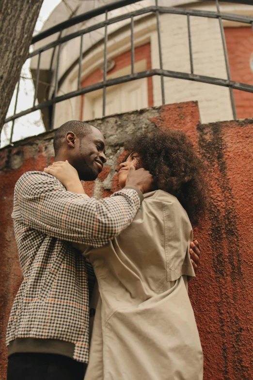 a man and woman standing next to each other in front of a building, pexels contest winner, hugs, with afro, 268435456k film, brown